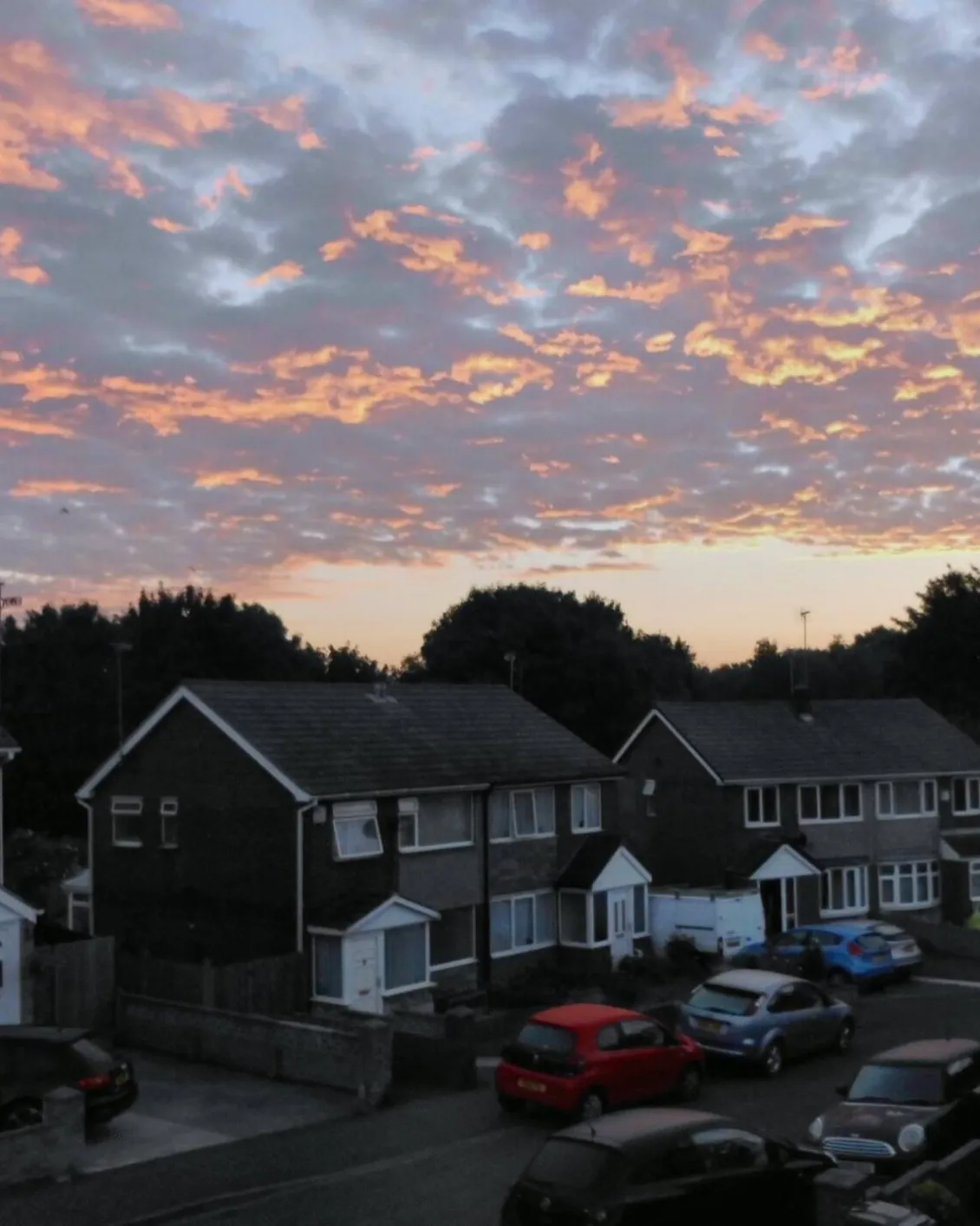 Sunrise over a street of semi-detached houses with cars parked outside.