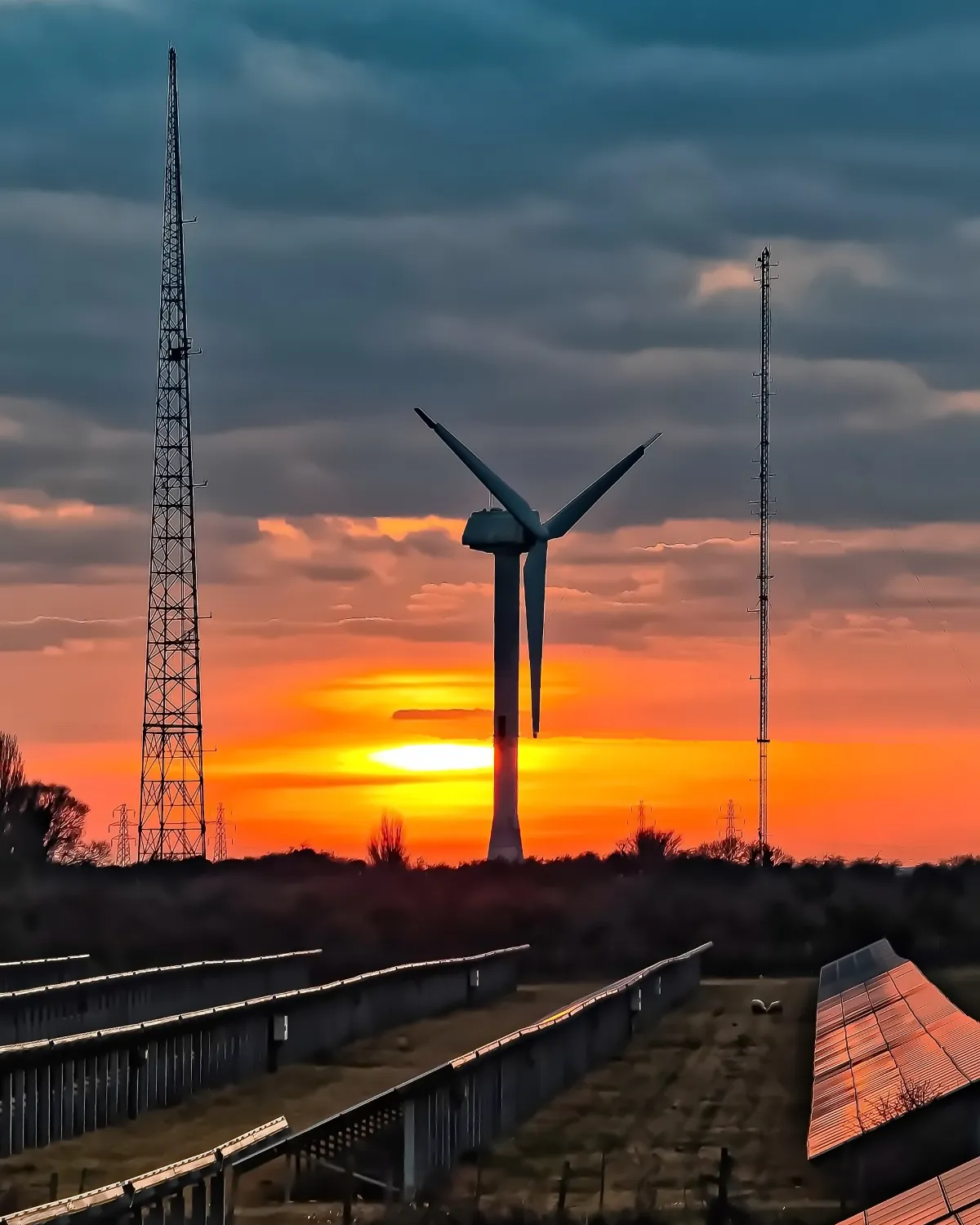 A wind turbine against an orange sunset, with solar panels in the field below, at Richborough in Kent.